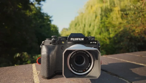 Fujifilm X-T5 camera body positioned next to a compact film camera on a road with tree-lined edges.