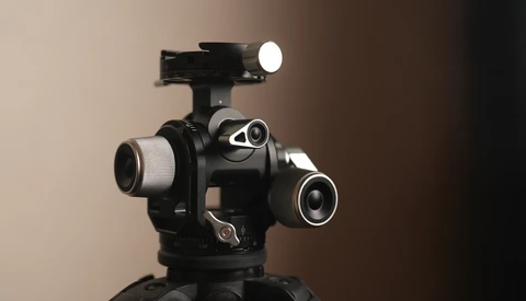Professional cinema camera head with multiple lens ports and mounted LED light on tripod.
