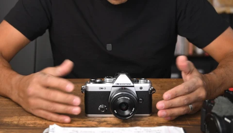 Hands presenting a vintage rangefinder camera on a wooden surface.