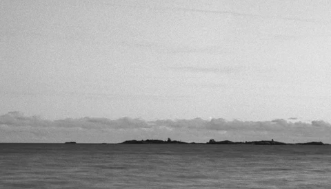 Minimalist black and white seascape with dark landmasses silhouetted against an overcast sky.