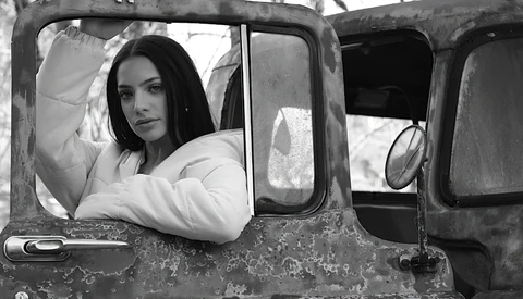 Woman in white jacket leaning out of vintage truck window in black and white portrait.