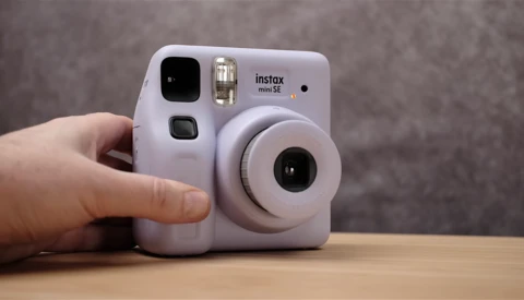 Lavender Instax Mini SE instant camera held in hand against neutral background.