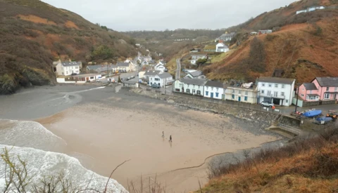 Coastal village nestled in a valley with sandy beach at low tide and residential buildings along the shoreline.
