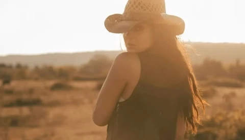 Woman wearing a cowboy hat standing in an arid desert landscape during golden hour.