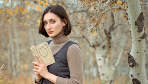 Woman holding an open book in an autumn forest with birch trees.