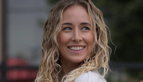 Young woman with wavy blonde hair smiling at camera outdoors.