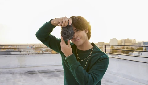 Photographer holding vintage film camera up to face on urban rooftop during golden hour.