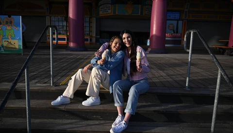Three young people sitting together on a shaded platform with colorful building columns in background.
