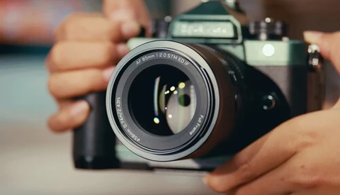 Photographer's hands holding a vintage SLR camera with lens extended, demonstrating proper grip and positioning.