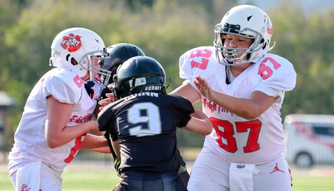 Youth football players in white and black uniforms competing for the ball during a daytime game.