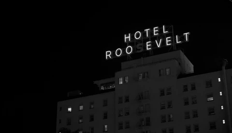 Hotel Roosevelt neon sign glowing on top of a dark multi-story building at night.