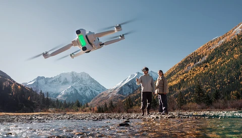 Drone flying over two people standing in a mountain valley stream.