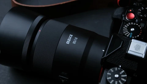 Matte black mirrorless camera with attached prime lens and visible control dials on dark surface.