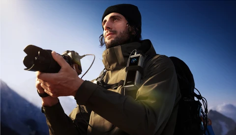 Male photographer holding a camera against a clear blue sky with mountains in the background.