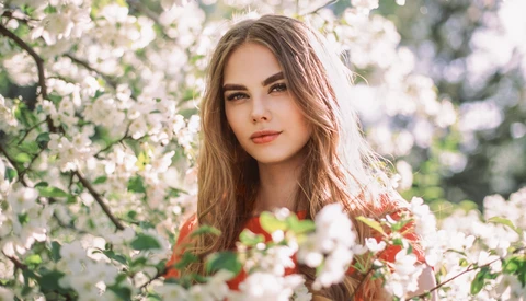 Woman with long brown hair surrounded by blooming white flowers in natural outdoor light.
