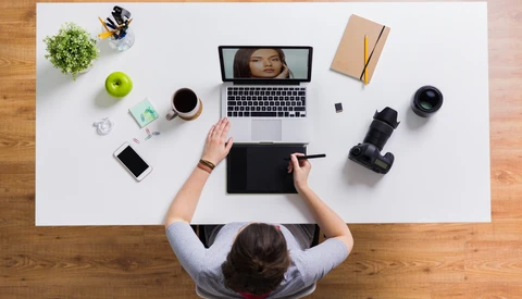 Overhead view of a creative workspace with a photographer using a graphics tablet at a white desk.