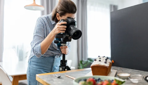 Food photographer shooting a styled flat lay setup with a DSLR camera on a tripod in a bright studio.