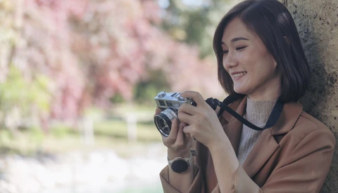 Woman holding a vintage film camera while smiling, with blooming flowers blurred in the background.