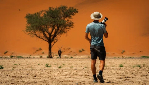 Runner jogging across desert landscape with acacia tree and orange sky.
