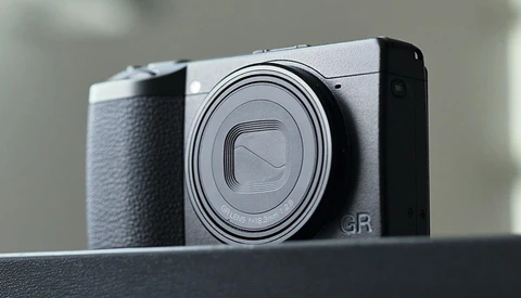 Ricoh GR compact camera with silver top plate and black grip, shown in three-quarter view against neutral background.