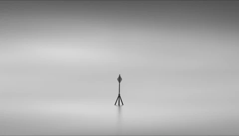 Solitary communication tower standing in fog with minimal ground visibility.