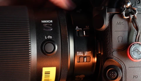 Nikon L-Fn lens with camera body and accessories in warm studio lighting.