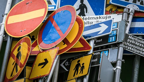 Stacked traffic signs with red no-entry circles and yellow warning signs featuring pedestrian symbols.