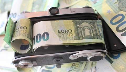 Vintage film camera wrapped in Euro banknotes, photographed on a surface covered with additional currency.