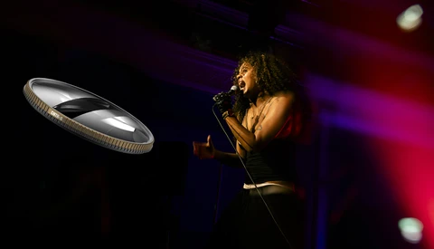 Singer performing at microphone with dramatic stage lighting and glowing circular light fixture.