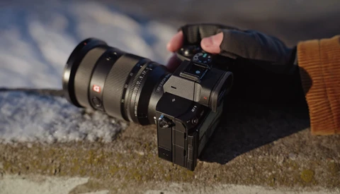 Mirrorless camera with wide-angle lens resting on sandy surface outdoors.