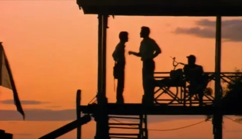 Silhouetted figures on a waterfront deck during golden hour sunset.