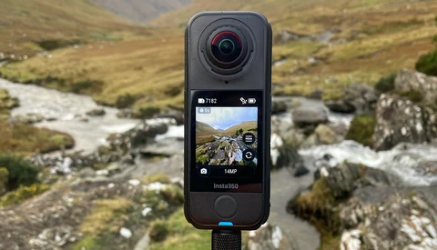 Insta360 action camera mounted on tripod displaying mountain stream landscape on rear screen.