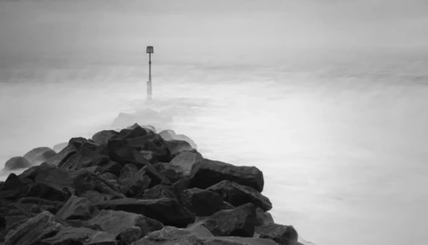 A communications tower rises from a rocky summit shrouded in mist and clouds.