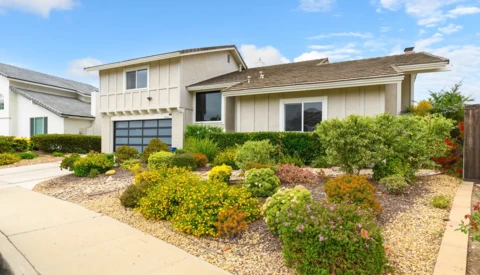 Contemporary two-story residential home with cream-colored siding, glass garage door, and drought-resistant landscaping.