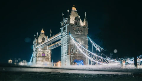 Tower Bridge in London illuminated at night with atmospheric mist surrounding its base.