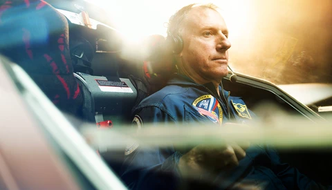 Pilot wearing headset in aircraft cockpit, backlit by golden sunlight streaming through windows.