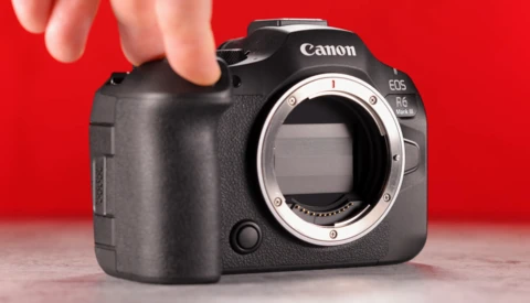 Canon EOS R6 Mark II mirrorless camera body held against red background, showing open mount without lens.