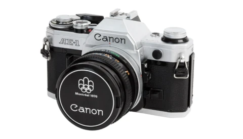 Canon AE-1 35mm SLR camera with silver top plate and black body, shown with standard lens and lens cap.