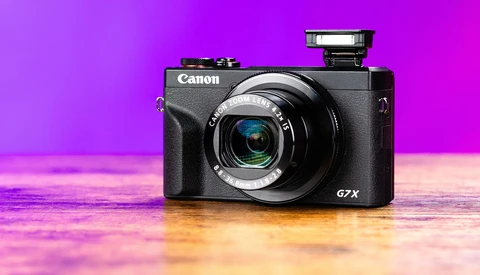 Canon PowerShot G7 X compact camera on reflective surface against vibrant magenta and gold gradient backdrop.