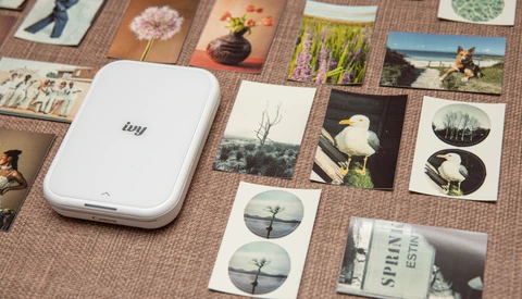 Portable photo printer surrounded by printed photos and contact sheets on a textured surface.