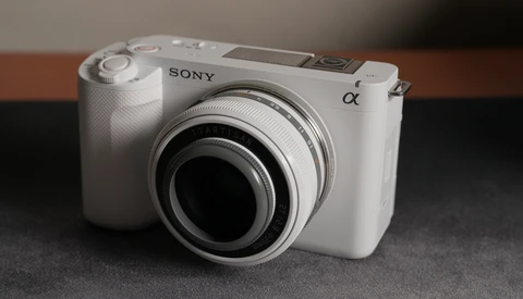 White Sony Alpha mirrorless camera with attached prime lens, shown from a three-quarter front view.
