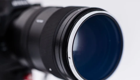 Close-up of a telephoto lens with a dark blue circular filter element and metallic focus ring against a white background.