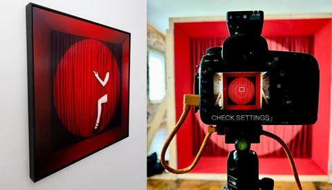 Red neon sign featuring a stylized figure in a phone booth, displayed on gallery wall and viewed through smartphone camera on tripod.