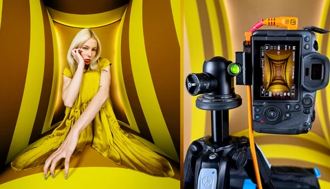 Studio setup with female model in yellow dress against striped backdrop, professional video camera on tripod in foreground.