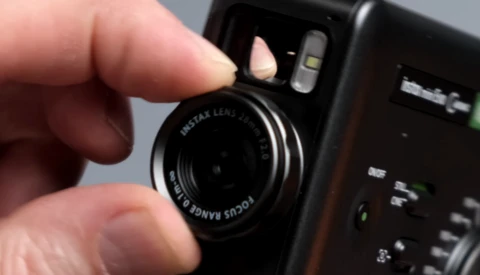 Hand holding a Fujifilm Instax instant camera with lens visible and flash unit mounted on top.