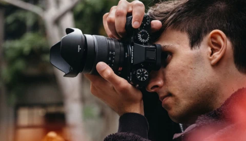 Male photographer holding a mirrorless camera to his face while focusing on a subject.