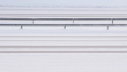 Aerial view of a snow-covered highway with guardrails and lane markings visible from above.