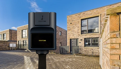 Electric vehicle charging station mounted on pole in residential street with brick buildings.