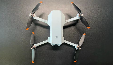 Overhead view of a compact white and gray drone with four propellers, displayed on a dark textured surface.