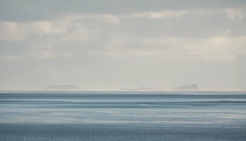 Calm seascape with distant headlands under overcast sky, horizontal layers of water and clouds.